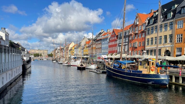 Old wooden boats in Copenhagen, moored in front of brightly painted warehouses.